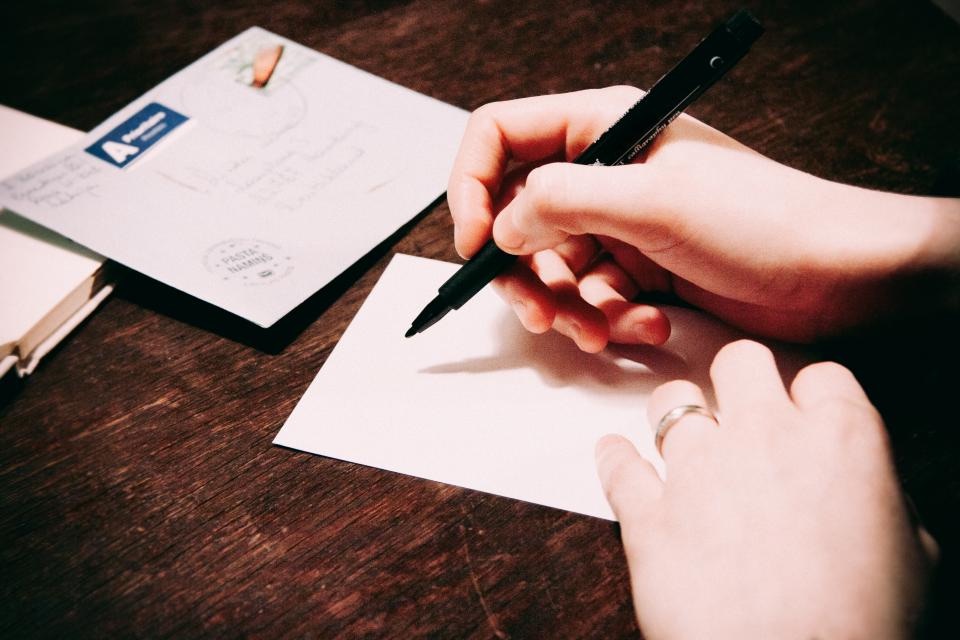 A volunteer handwriting a postcard at a wooden table